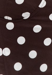 Gros plan sur un tissu marron foncé à gros pois blancs avec une couture courbée visible.