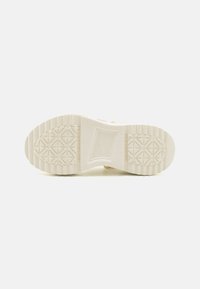 Suela de una zapatilla deportiva, de un color crema claro, texturizada con un patrón de diamante, que presenta un área central suave con la marca.