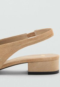 Beige suede sandal with a mid stacked heel, open back, and thin straps; features contrast stitching on the upper and a smooth sole.