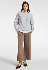 Harmaa kaapeli-neulepusero, jossa on ribattu helma, on kerrostettu vaaleansinisen kauluspaidalla. Ruskeat leveät housut ja tummanruskeat avokkaat.