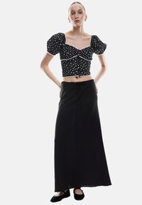 Sort blomster crop top med puffærmer, blondekant, parret med en lang sort nederdel med snøre i taljen, båret med sorte flade sko.
