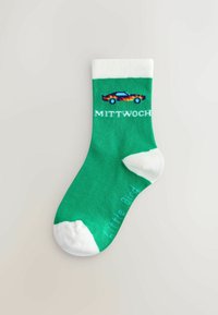 Calze verdi con risvolto e punta bianchi, decorate con una grafica di un'auto colorata e il testo "MITTWOCHE". Il materiale è una maglia liscia, dal design casual.