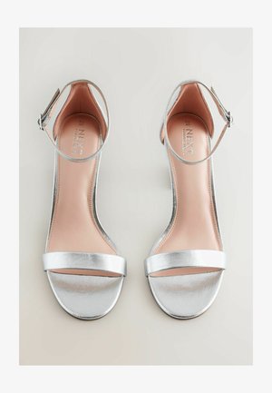 Silver high-heeled sandals with a smooth metallic finish, open toe, ankle strap, and a flat, textured sole. Cushion-like insole in light beige.