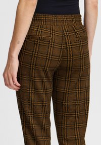 Braun und schwarze karierte Hose mit elastischem Bund. Verfügt über einen strukturierten Stoff und zwei Gesäßtaschen, die eine maßgeschneiderte Passform zeigen.