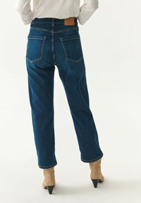 Temno modre jeans hlače s ravnim fitom, opremljene z rjavim usnjenim zamaškom na pasu in dvema zadnjima žepoma s podrobnostmi šivanja.