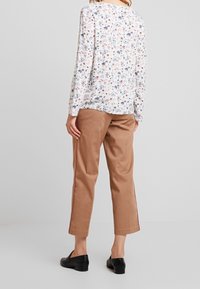 Blusa blanca con estampado floral y mangas largas, combinada con pantalones cortos color tostado. Zapatos negros sin cordones completan el conjunto.