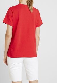 Rød kortærmet t-shirt lavet af bomuld, med rund halsudskæring og en afslappet pasform, parret med hvide denimshorts med flossede kanter.