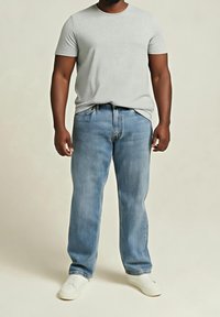 Szary t-shirt z krótkim rękawem, jasnoniebieskie jeansy o prostych nogawkach oraz białe buty wsuwane. Gładka faktura bez widocznych wzorów ani elementów metalowych.