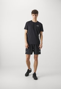 Čierne atletické tričko a šortky vyrobené z ľahkej tkaniny. Obsahujú logo na hrudi a elastický pás na šortkách.