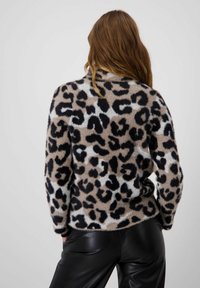 Leopardenmuster-Pullover aus weichem, plüschigem Stoff; sandfarbener Hintergrund mit schwarzen und weißen Flecken. Kombiniert mit glänzenden schwarzen Hosen; lässige Passform.