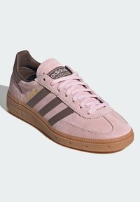 Sneakers de camurça rosa com detalhes em pele castanha, três riscas castanhas, sola de borracha texturizada e detalhe da língua com marca.