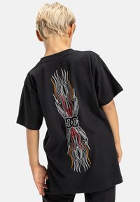 Camiseta de algodón negra con un diseño de llamas coloridas en la parte posterior, con un acento de logotipo en el centro. Manga corta, corte relajado.