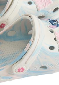 Vita träskor med ett marmorerat blått och rosa mönster, prydda med en blommig dekoration och en karaktärsdesign på sidan. Perforerade för andningsförmåga.