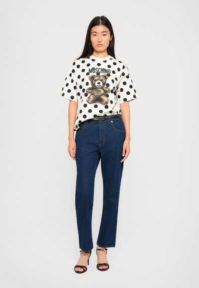 White t-shirt with black polka dots and teddy bear graphic; paired with dark blue straight-leg jeans and black strappy heels.