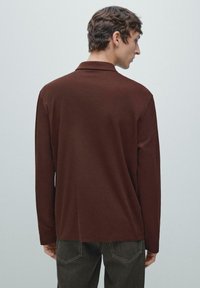 Brązowa koszulka polo z długim rękawem, klasycznym kołnierzykiem, miękką fakturą, prostym krojem oraz starannym wykończeniem na linii dołu i mankietach.