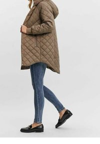 Parka marrón acolchada con capucha, cremallera lateral y cierre de botones a presión. Se lleva sobre vaqueros azules y mocasines negros con detalles texturizados.