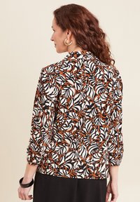 Lange mouwen blouse met een zwart, wit en oranje bladerenpatroon, voorzien van een ronde halslijn en licht gatherende mouwen.