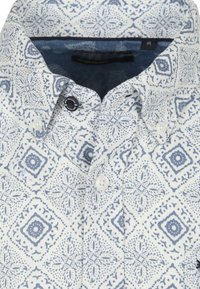 Een button-up shirt van witte stof met blauwe ingewikkelde patronen. Voorzien van een puntige kraag en witte knopen, met een gladde, katoenachtige textuur.