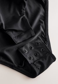 Nahaufnahme eines schwarzen Stoffs mit elastischen Kanten und einem Druckknopfverschluss mit sechs schwarzen Druckknöpfen.