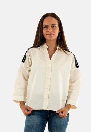 Camicia bianca con bottoni, spalle a strisce nere, realizzata in un tessuto leggero. Ha una vestibilità comoda e maniche lunghe.