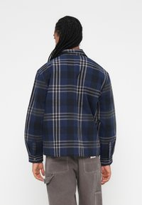 Camisa aos quadrados em azul marinho com padrões cinza e preto; mangas compridas e gola; feita de tecido suave; ajuste descontraído; detalhe de punho com botão.