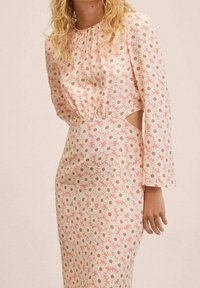 Vestido de manga larga con un escote alto, que presenta un patrón floral de margaritas blancas y acentos melocotón sobre un fondo claro. Detalle de corte lateral.