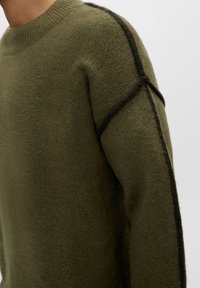 Sweter dzianinowy w oliwkowej zieleni z okrągłym dekoltem, z teksturowanej tkaniny, kontrastującymi czarnymi szwami po bokach oraz luźnym krojem.