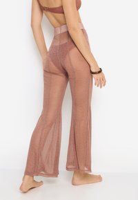 Ροζ χρυσό διαφανές παντελόνι με φαρδιά καμπάνα, υψηλή μέση, λαμπερή υφή και διαφανές σχέδιο που εκτείνεται μέχρι τους αστραγάλους.