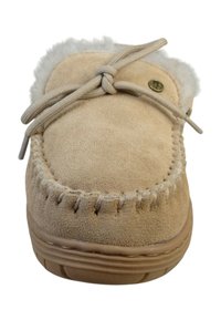 Pantufla mocasín de ante beige con bordes cosidos, suela marrón claro, forro de piel de pelo y lazo a juego atado en la parte superior.