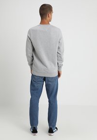 Sudadera gris de manga larga y cuello redondo, combinada con jeans de mezclilla azules y zapatillas en blanco y negro. Textura de tela suave.