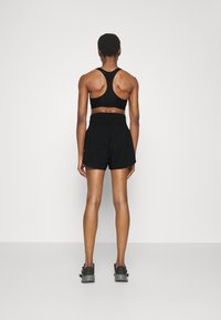 Sujetador deportivo negro con diseño de espalda nadadora, combinado con pantalones cortos negros con cinturilla elástica. El modelo lleva zapatillas deportivas negras.