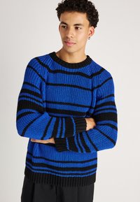 Pull en tricot avec des rayures horizontales bleues et noires, col ras du cou, poignets et ourlet côtelés, texture moyenne et coupe décontractée.