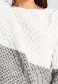 Sweter dziany o prążkowanej fakturze z białą górną częścią i szarą dolną, prezentujący kontrast kolorów i materiałów.