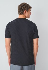 Sort T-shirt med korte ærmer og et tekstureret geometrisk mønster. Rund halsdesign, blødt stof og en tætsiddende pasform.