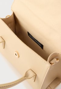 Μπεζ τσάντα χειρός από συνθετικό υλικό με λεία υφή, κλείσιμο με πάτημα και εσωτερική ετικέτα με μαύρα γράμματα. Οι λαβές είναι ραμμένες.