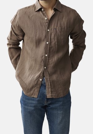 Bruine linnen langemouwhemd met knopen, een borstzak en een relaxte pasvorm. Gecombineerd met blauwe denim jeans. Textuur zichtbaar.