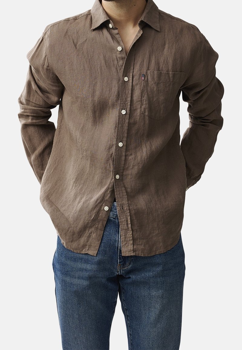 Hnědá lněná košile s dlouhým rukávem, knoflíky, náprsní kapsou a volným střihem. V kombinaci s modrými džíny. Viditelný strukturovaný povrch.