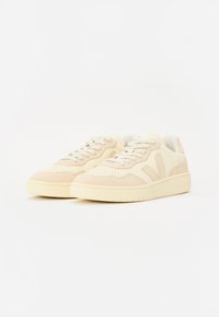 Világos bézs sneaker, amely sima és velúr textúrák keverékéből készült. Lekerekített orr, perforált díszítések és fűzős kialakítás. Vastag gumi talp.
