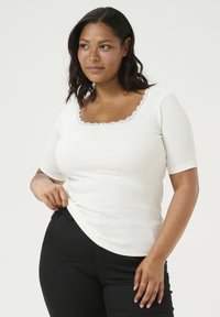 Haut blanc à manches courtes avec un col carré, agrémenté de délicates garnitures en dentelle et d'un petit nœud au centre. Assorti à un pantalon noir.