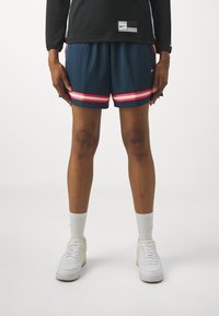 Nike sportlikud lühikesed püksid tumesinises värvitoonis roosa ja valge triibuga, millel on tekstureeritud materjal ja mis on kokku sobitatud valgete tossude ja sokkidega.