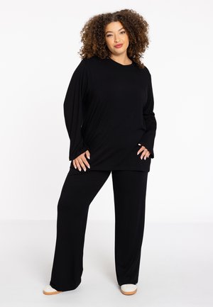 Schwarzes Loungewear-Set bestehend aus einem locker sitzenden Langarmshirt und weit geschnittenen Hosen, gefertigt aus einem weichen Stoff mit glatter Textur.