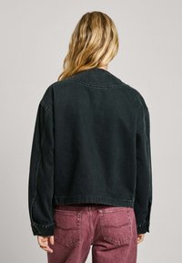Schwarze Jeansjacke mit lässigem Schnitt, mit spitzem Kragen, langen Ärmeln und Knopfdetails an den Bündchen, kombiniert mit pinken Jeans.
