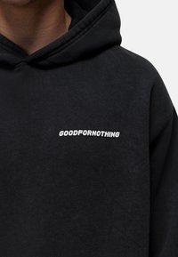 Felpa nera con cappuccio realizzata in tessuto morbido, con logo "GOODFORNOTHING" ricamato in bianco sul davanti. Include un cappuccio oversize e polsini a costine.