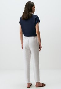 Haut en coton bleu marine à manches courtes associé à un pantalon en lin blanc. Les deux vêtements sont de coupe décontractée, avec une texture unie et un minimum de détails.