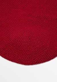 Close-up of a red knitted fabric with a circular pattern on a white background.