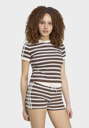 Ung kvinde med krøllet hår iført en stribet kortærmet skjorte og matchende shorts med hvidt Adidas logo med tre striber.