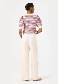 Gestreiftes, kurzärmliges Strickoberteil in Rot, Blau und Weiß; kombiniert mit kremfarbenen, gerippten weiten Hosen. Flache Sandalen vervollständigen den Look.