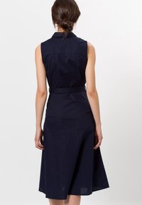 Robe bleu marine sans manches avec col, taille cintrée et jupe évasée. Fabriquée dans un tissu léger à texture lisse.