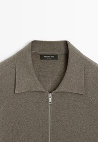 Brauner Reißverschluss-Pullover mit geripptem Textur, mit einem breiten Kragen und einem silbernen Reißverschluss. Das Etikett trägt die Aufschrift "Massimo Dutti."
