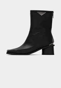 Stivale ankle in pelle nera con punta appuntita, tacco a blocco di altezza media e dettagli del logo in tonalità argentata vicino alla cerniera sul retro.